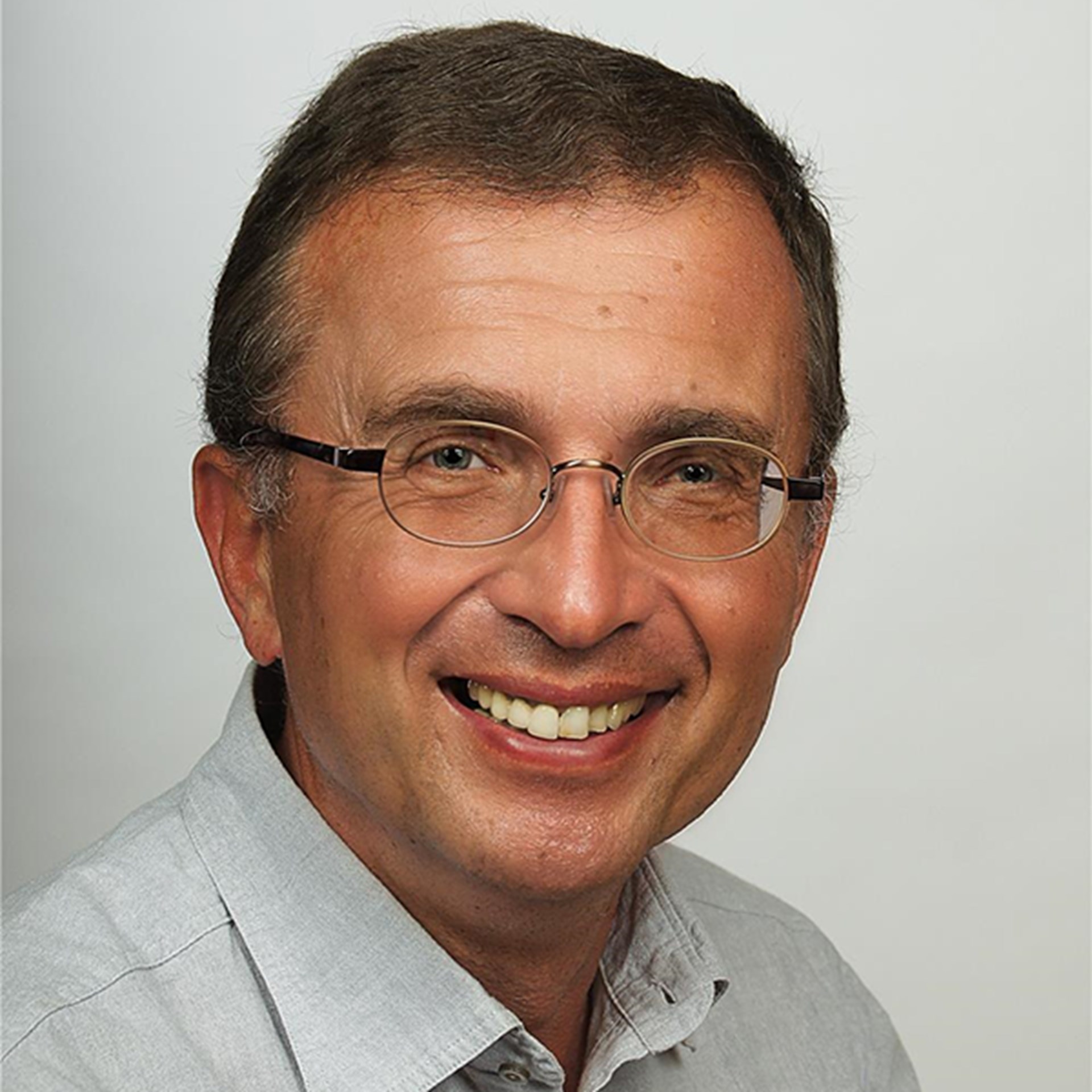 Lächelnder Mann mit braunen Haaren und Brille, der ein graues Hemd trägt