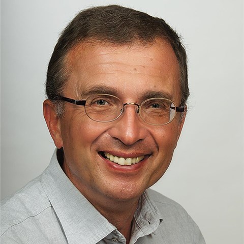 Lächelnder Mann mit braunen Haaren und Brille, der ein graues Hemd trägt