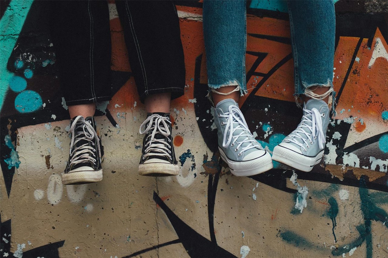 Symbolfoto zur Armutswoche 2026: Füße mit Turnschuhen dran - ein Paar neu und schick, das zweite Paar Schuhe abgelaufen und schmutzig. 