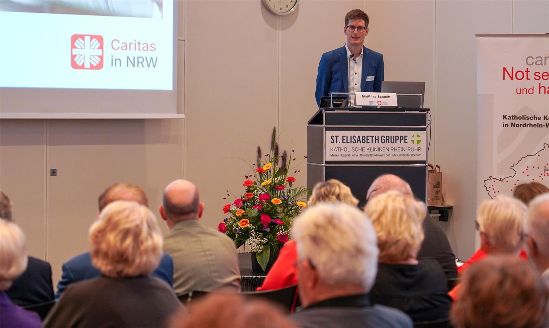 Matthias Schmitt am Sprechpult vor den Zuhörenden. 
