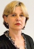 Frau mit hellblonden Haaren, die eine schwarze Jacke mit gemustertem Rand trägt