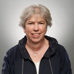 Lächelnde Frau mit grauen Haaren, die eine dunkle Kapuzenjacke und ein weißes Shirt trägt