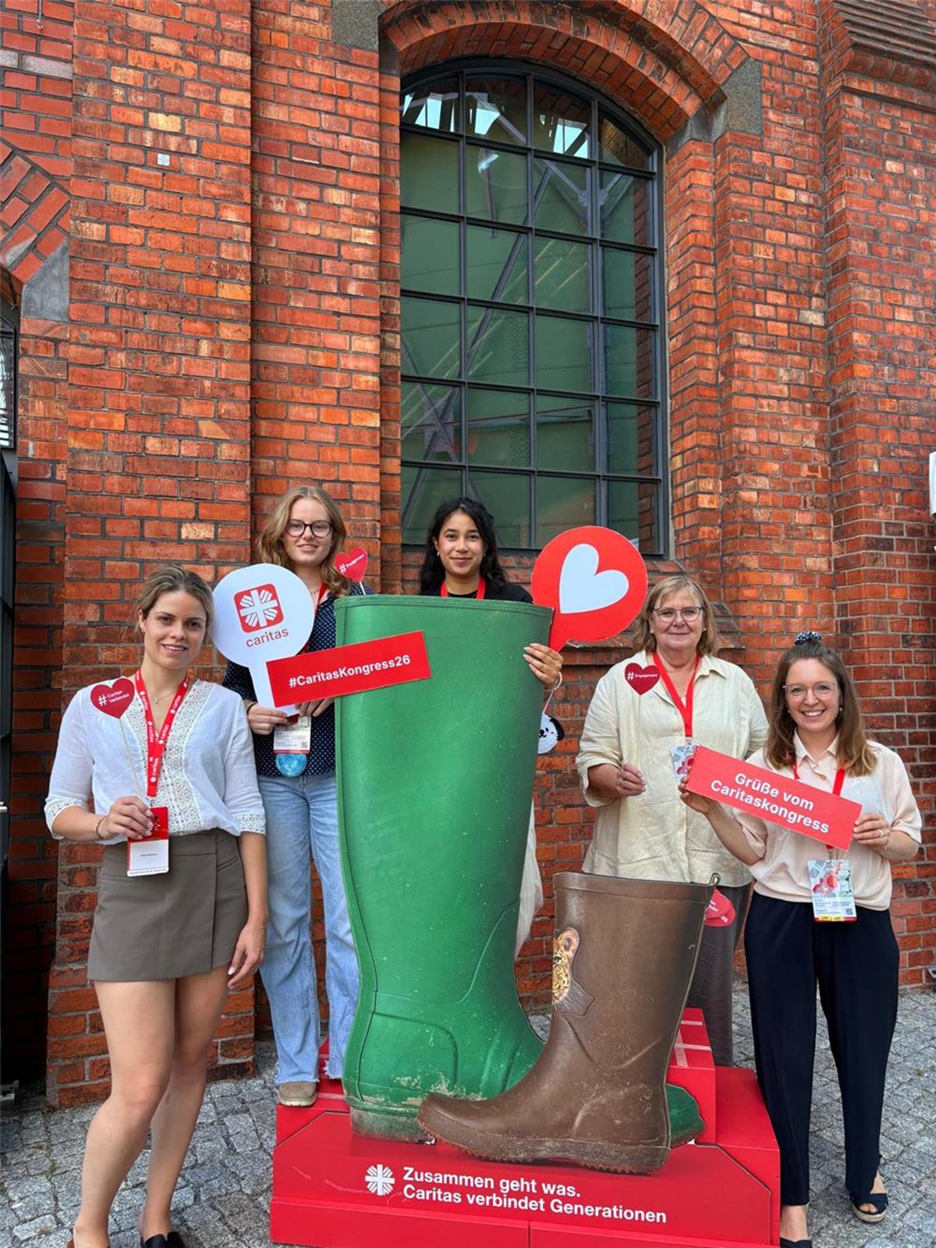 Besucherinnen des Caritas-Kongresses stehen zum Gruppenfoto um einen Pappaufsteller - ein großer, grüner Stiefel und ein kleiner brauner Kinderstiefel. 
