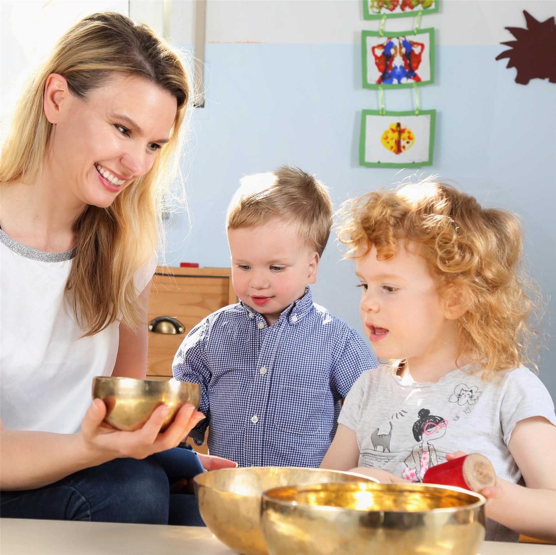 Frau zeigt zwei Kleinkindern Klangschalen